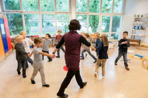 Lehrperson bildet mit Kindern einen Kreis im Schulzimmer